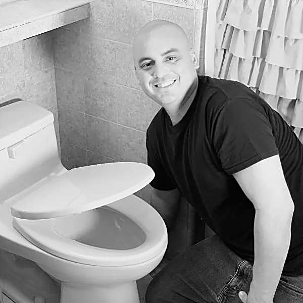 Danny kneeling beside a newly set toilet in a finished bathroom.