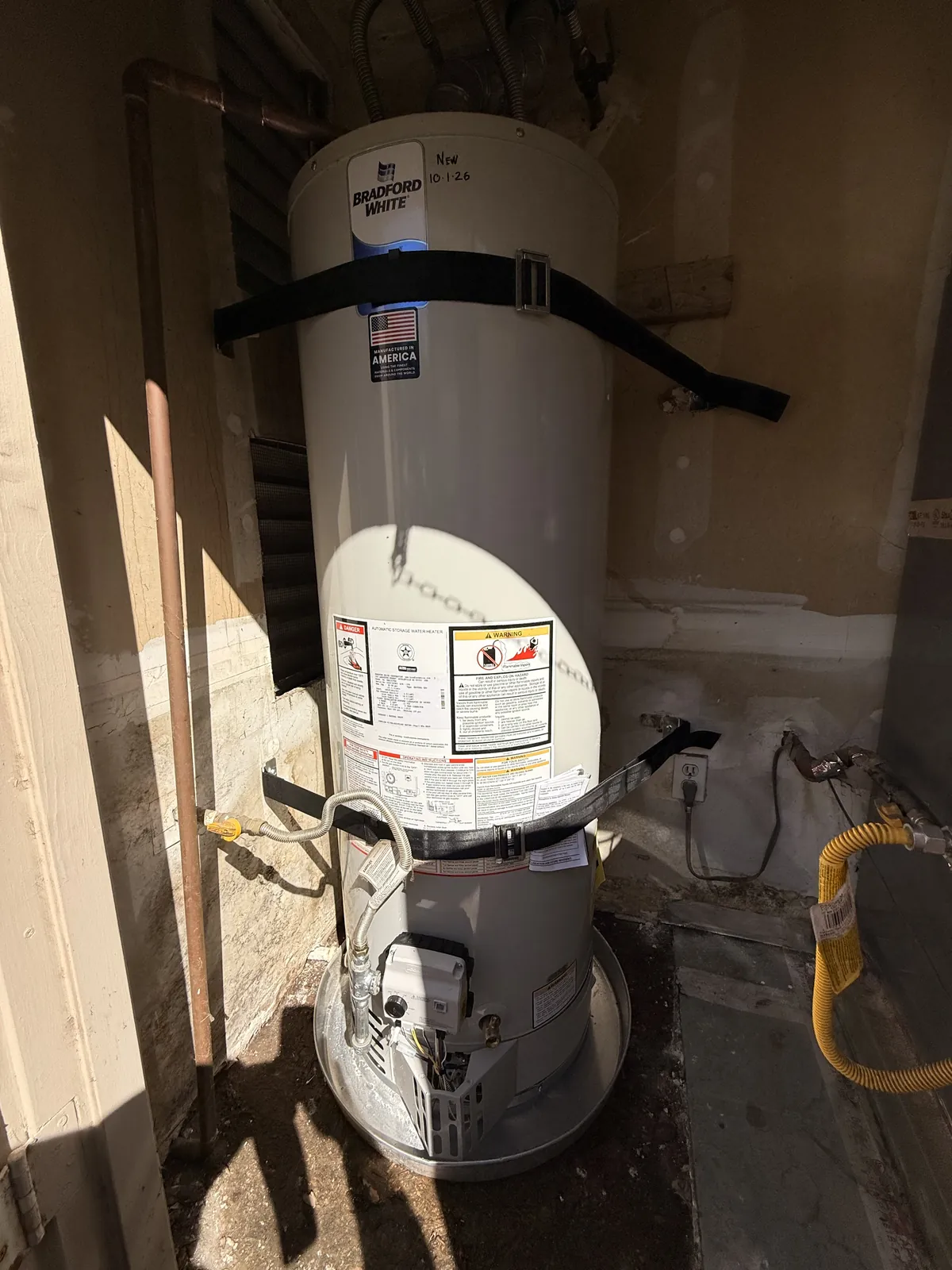 The new 40-gallon Bradford White, strapped, with new flex lines and a sediment trap