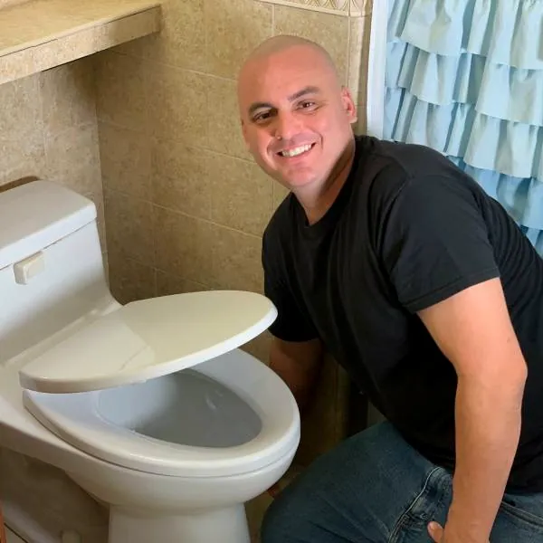 Dan kneeling beside a newly set toilet in a finished bathroom.