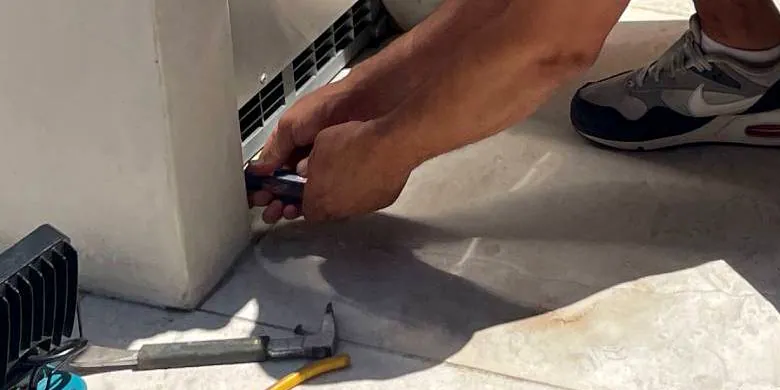 Close on Dan's hands driving a screwdriver, with a work light, hammer and pliers laid out on the concrete.